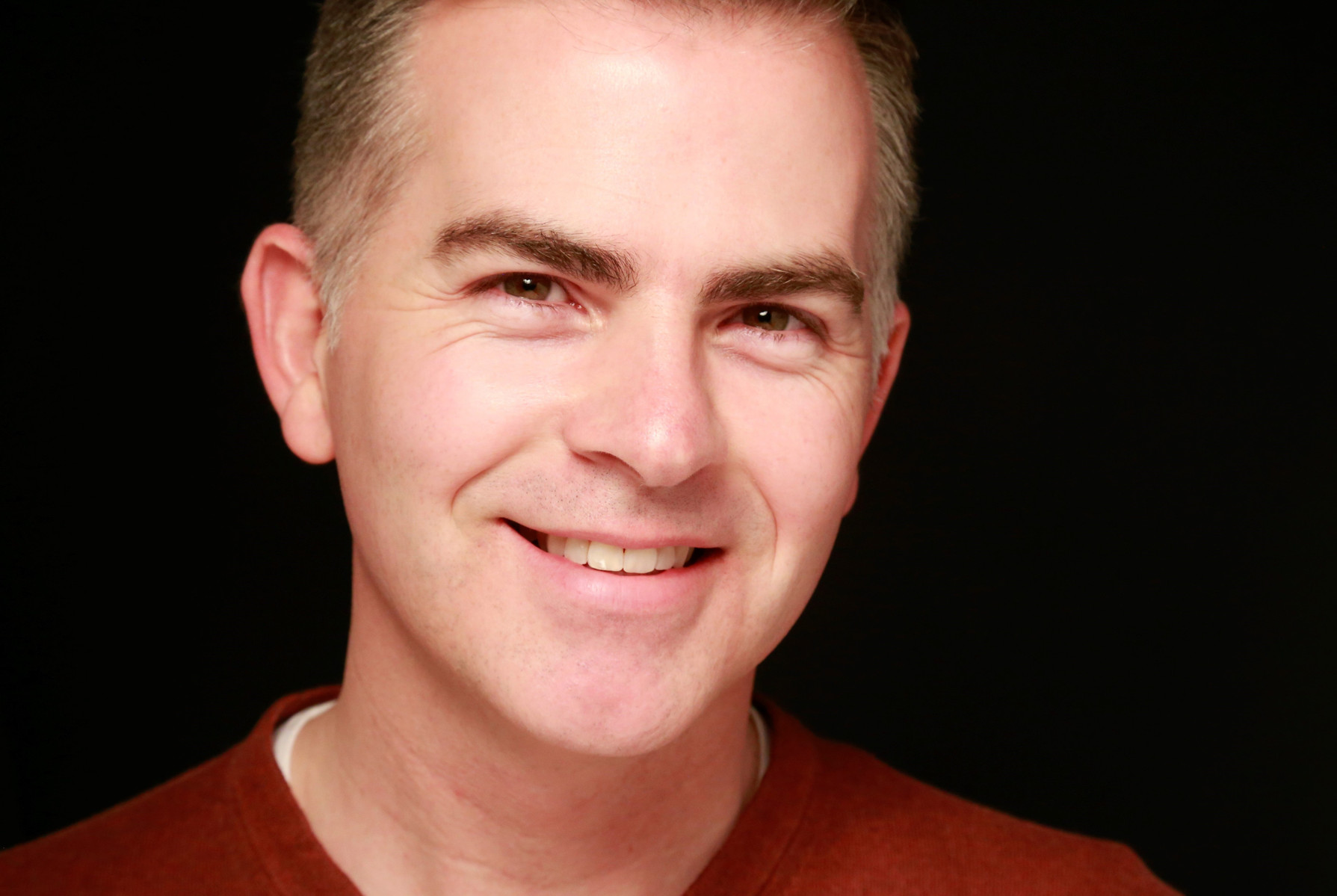 Professional Headshot of a man wearing a red top against a black background
