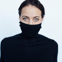 Contemporary portrait of a woman wearing black polo neck turtle neck jumper pulled over her mouth, with striking blue eyes. 