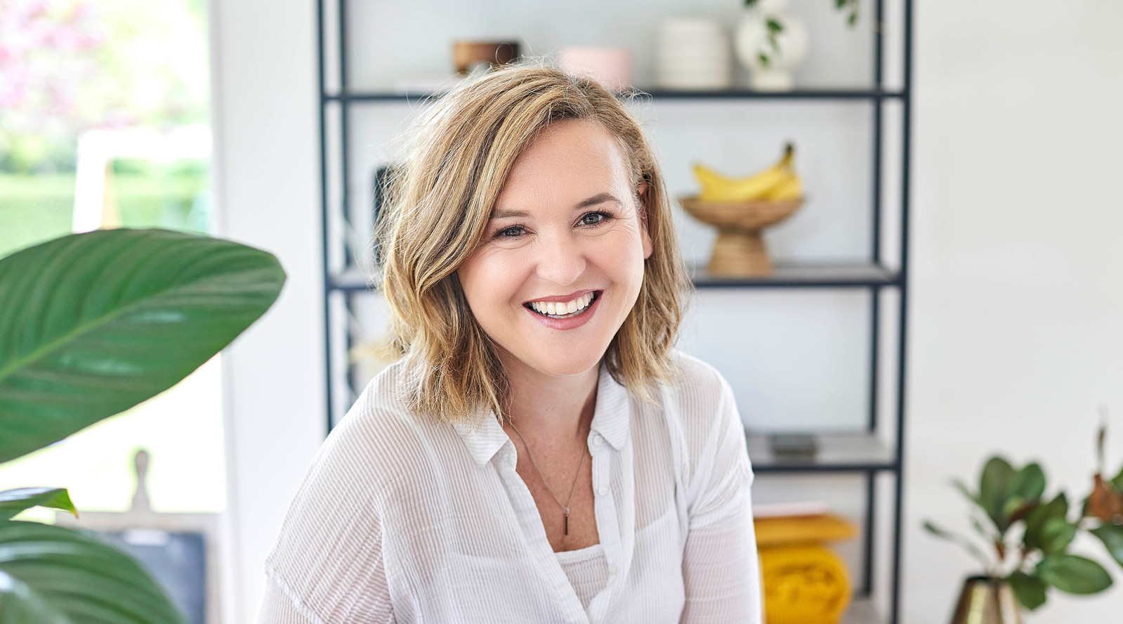 personal branding commercial image of women smiling at camera with plant and bookshelf in background