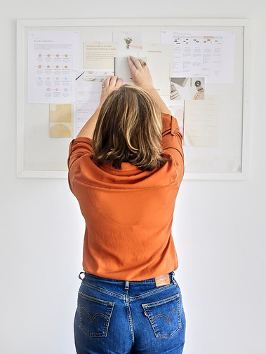 personal branding image of a women with a pinboard planning.  orange top, brand photographer