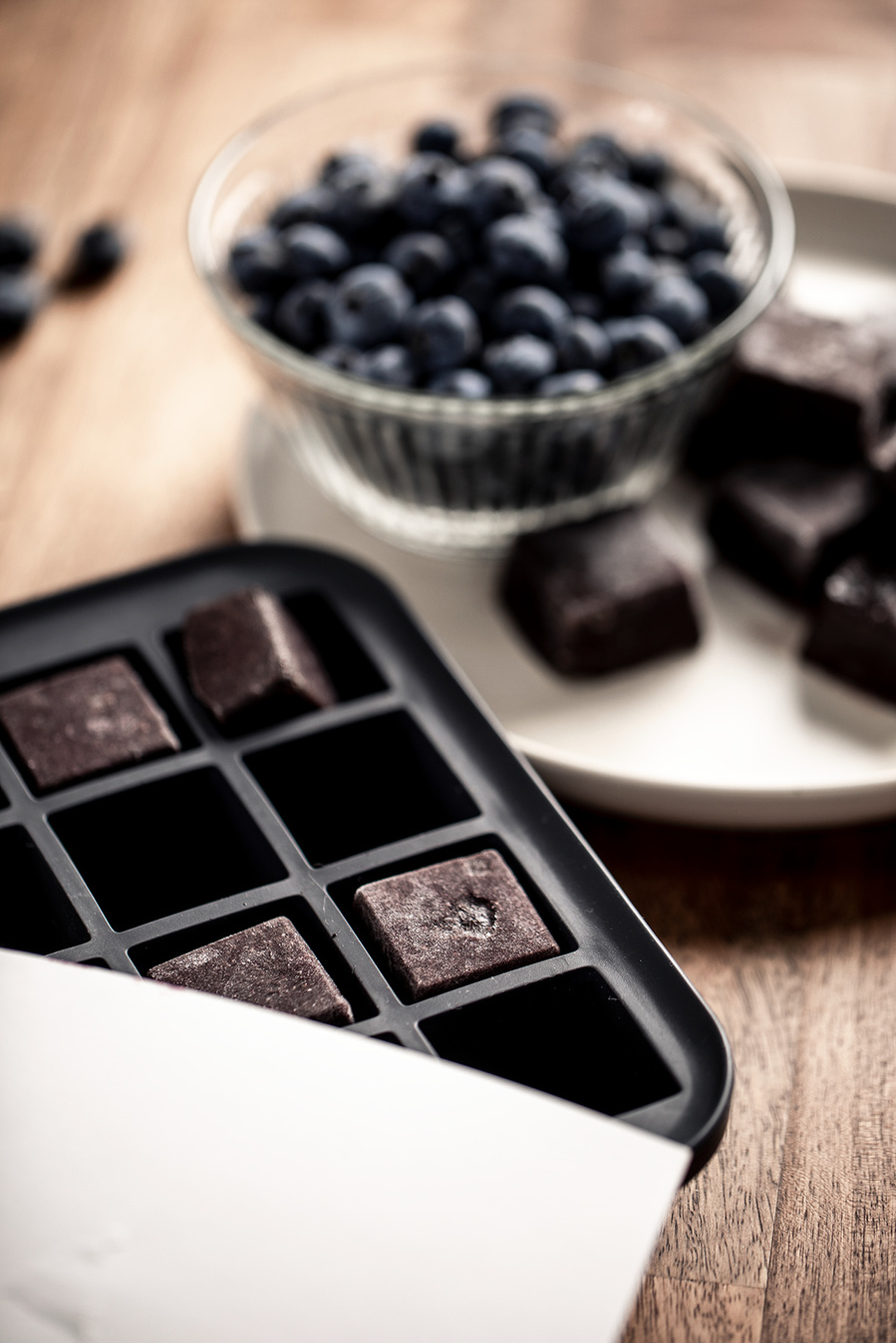 Silicone ice cube tray with frozen blueberry smoothie starters in it. Plate with some of the cubes and a bowl of fresh blueberries in the background. Images of blueberries for the blueberry council. 