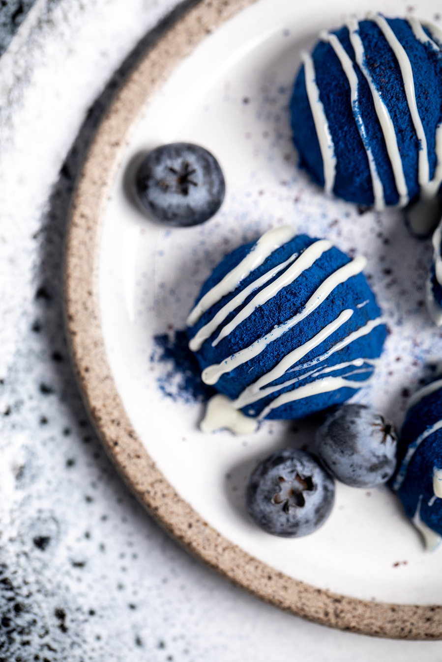 Vibrant blueberry dusted truffles with white chocolate drizzle on a stoneware plate with extra fresh blueberries