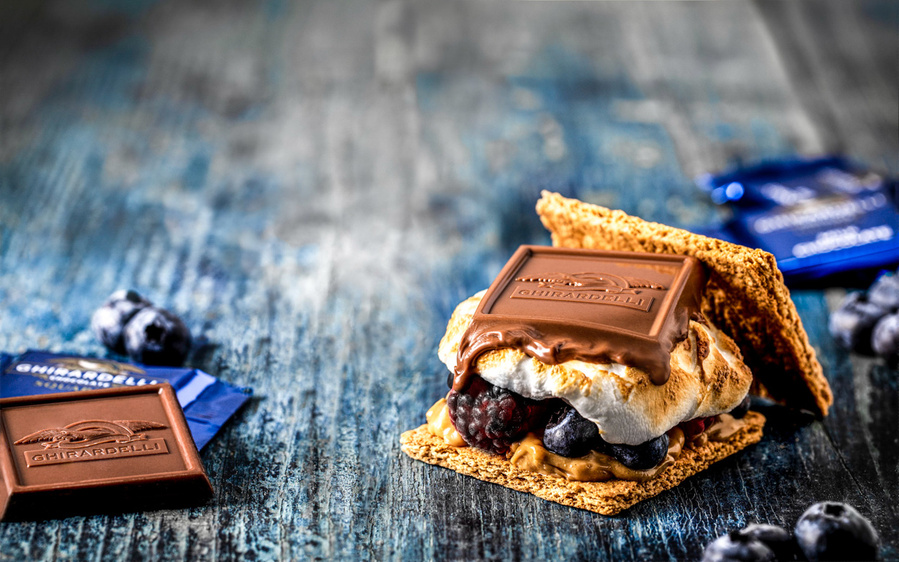 Macro chocolate photography of a Ghirardelli s'more with toasted marshmallows, blackberries, and blueberries. 
