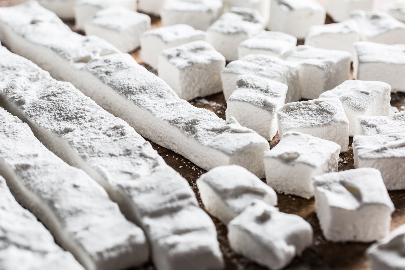 lines of homemade marshmallows being cut into cubes on a wood surface for hot drink photography