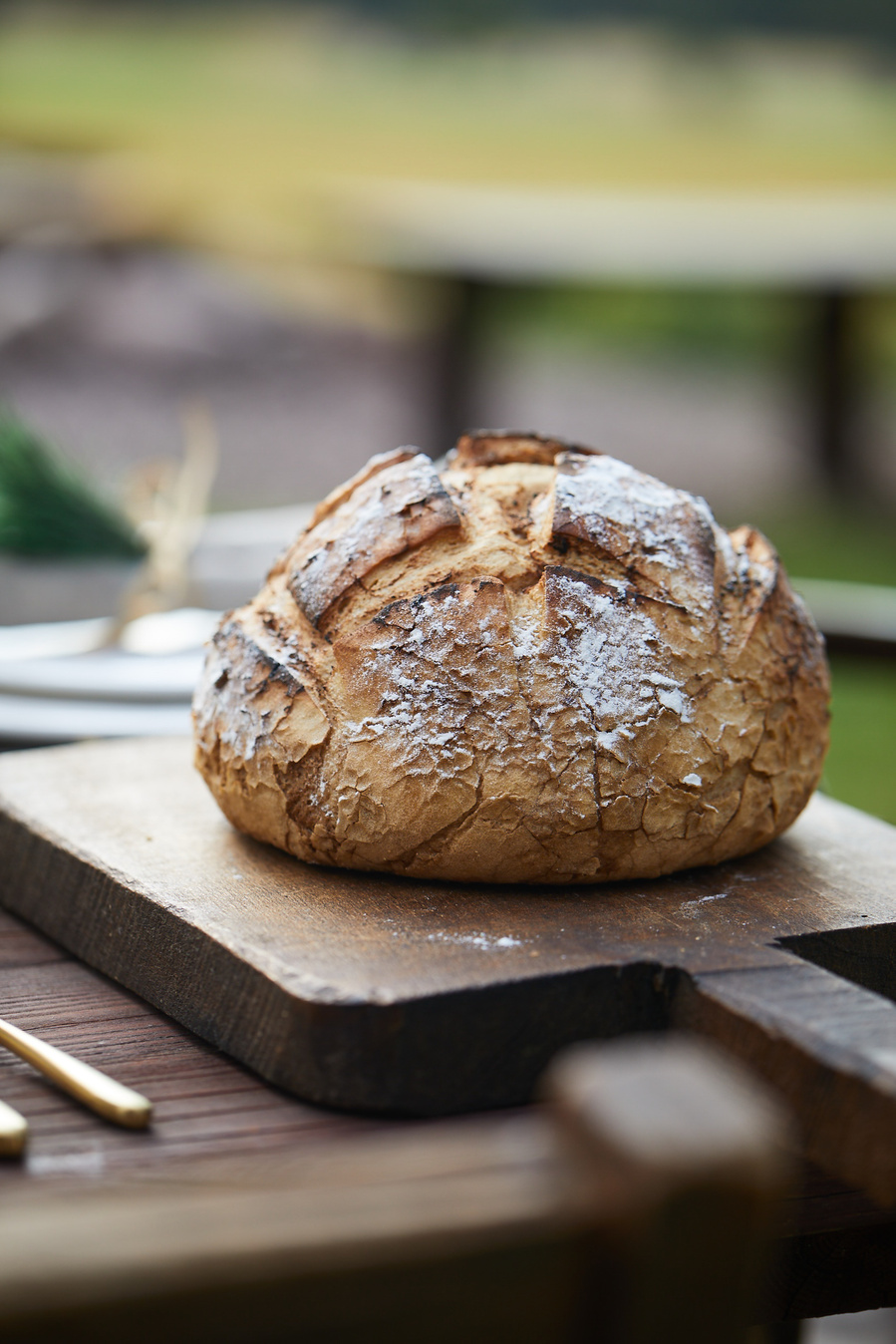 Loaf of rustic bread on a wooden cutting board. Set on a picnic table of a glam outdoor dinner party. 