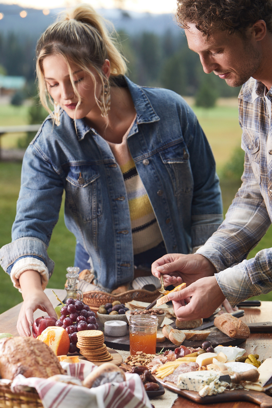 Two fashion models reach for food over a outdoor picnic table dinner party setup. Photography of food for lifestyle food photography for The Buckle