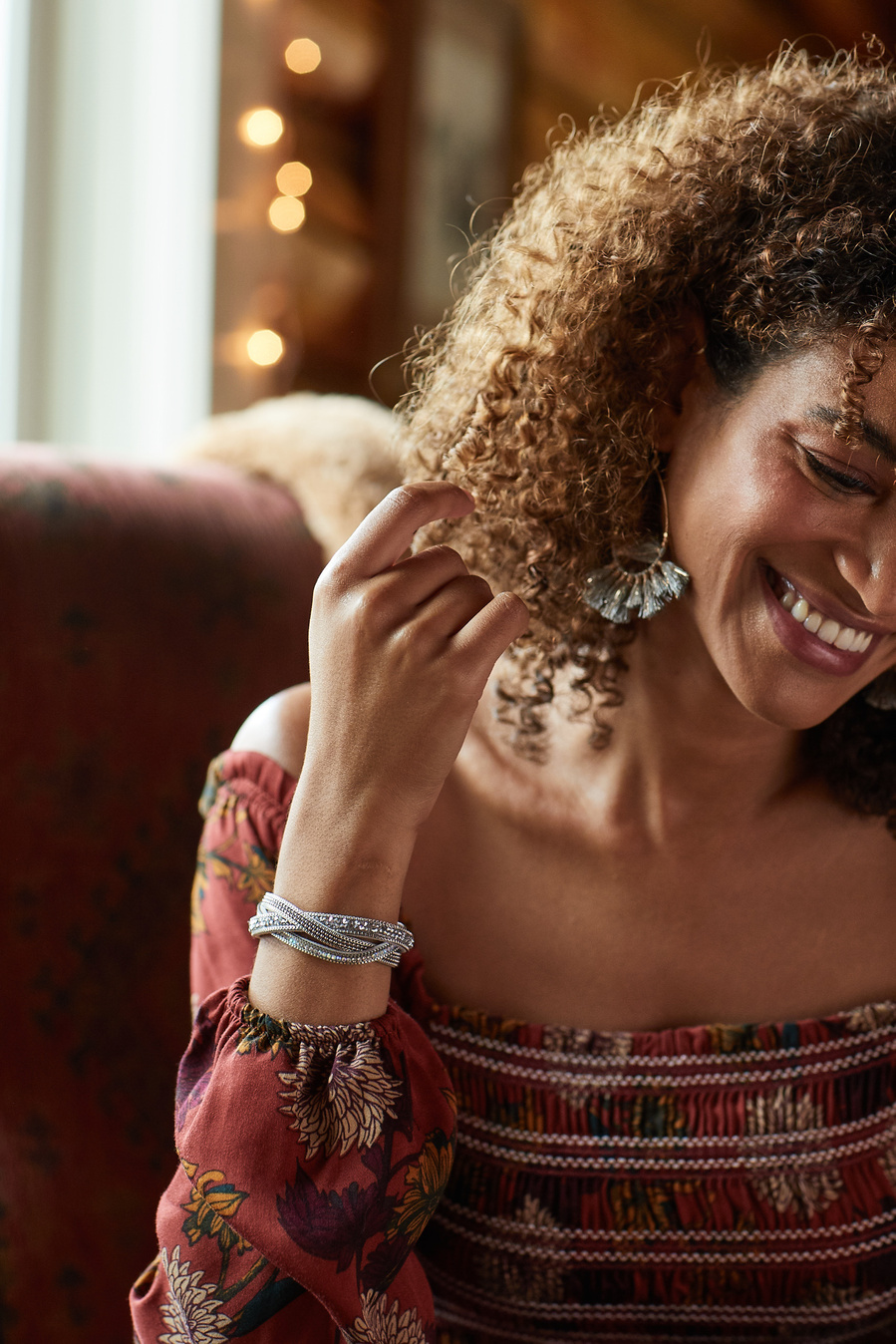 Female fashion model shows off red peasant top, bracelet and earrings with hand in her hair. Fashion lifestyle photography for The Buckle