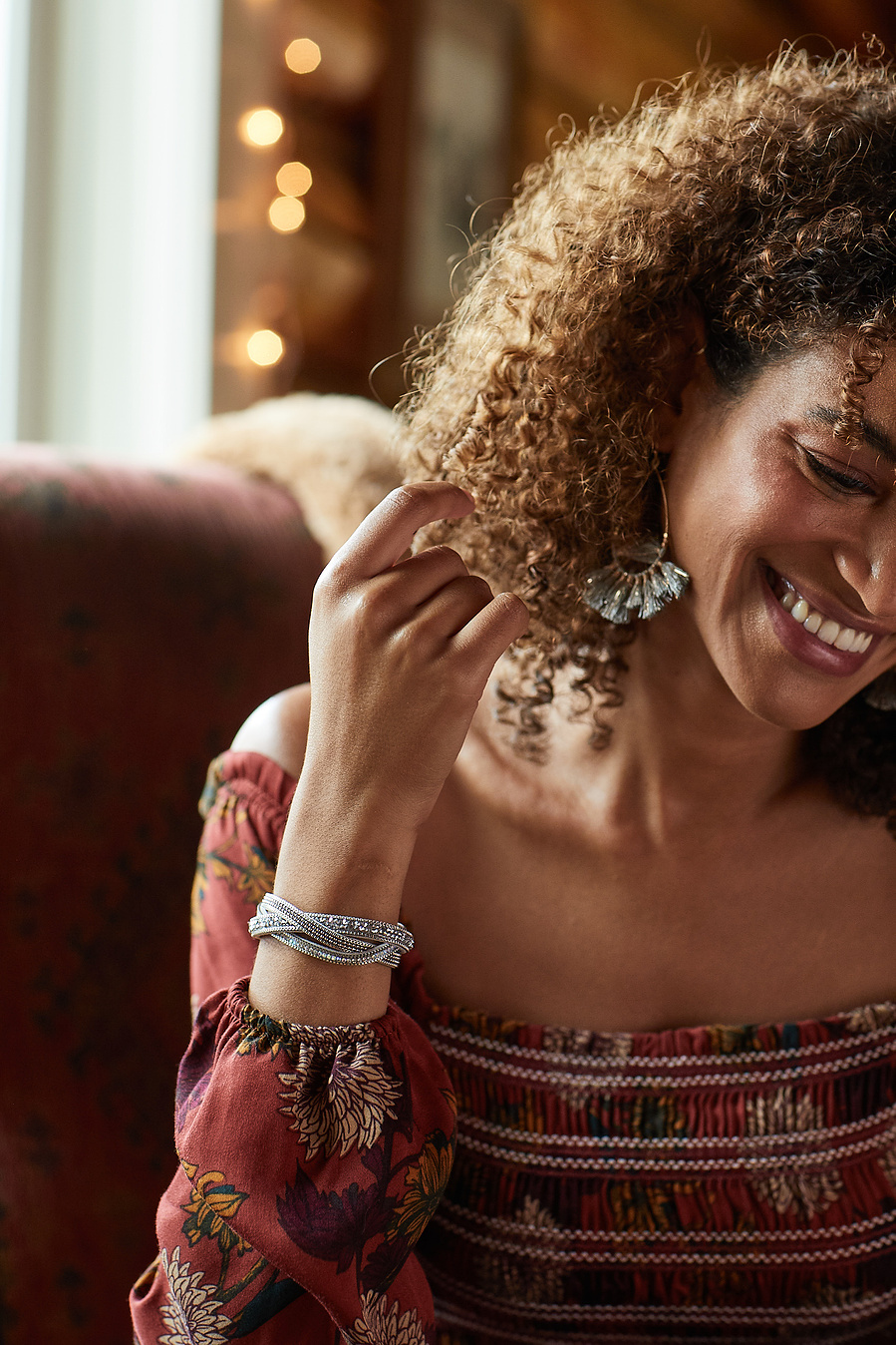 Female fashion model shows off red peasant top, bracelet and earrings with hand in her hair. Fashion lifestyle photography for The Buckle