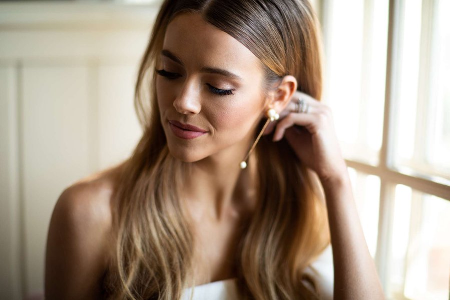 bride near a window looking away from the light with hand in hair showing gold earrings
