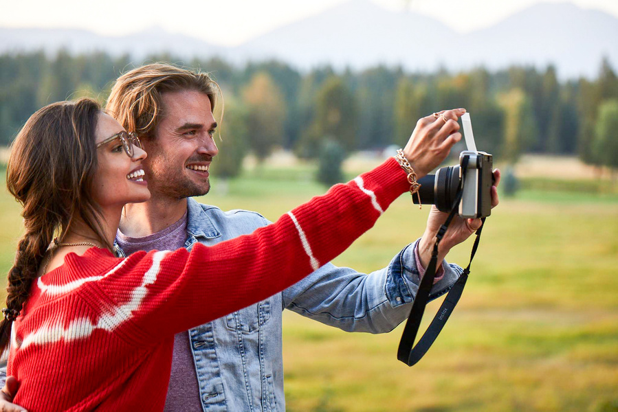Two models in casual fall clothing make a selfie with an old camera with a strap. Lifestyle fashion photography for The Buckle