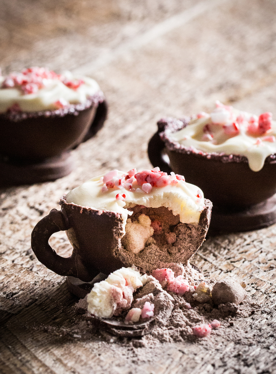 Set of three chocolate cups filled with hot cocoa mix and peppermint for drink photography. The cup in front is broken open so you can see the inside. 