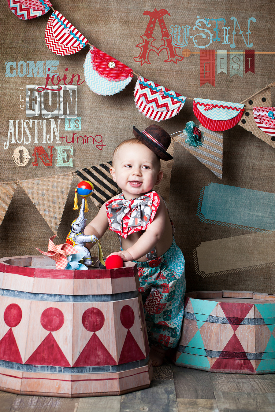baby boy in clown costume with vintage painted barrels and circus decorations for birthday party event photography. 