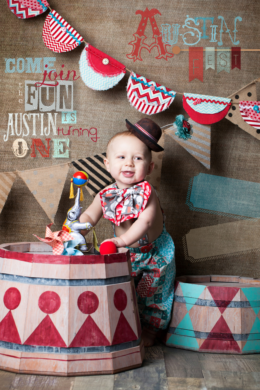 baby boy in clown costume with vintage painted barrels and circus decorations for birthday party event photography. 