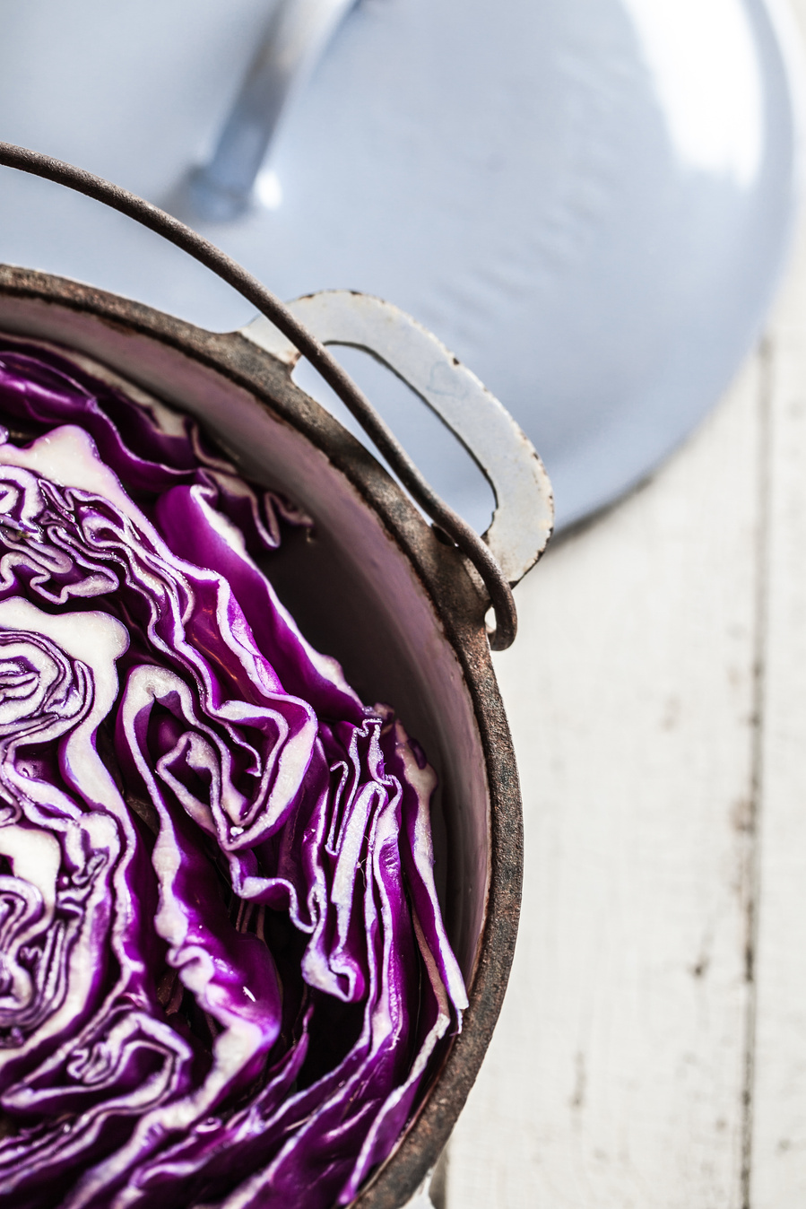 Halved red cabbage in a metal pot with a handle and the lid on the surface behind. Process shot for diy blue cabbage dyed eggs photography. 