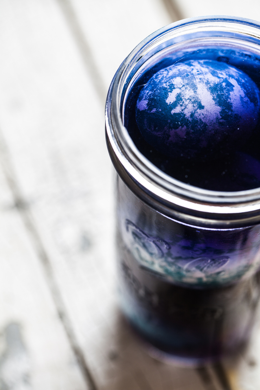 Overhead images of hard boiled egg in skinny mason jar filled with blue cabbage dye. 