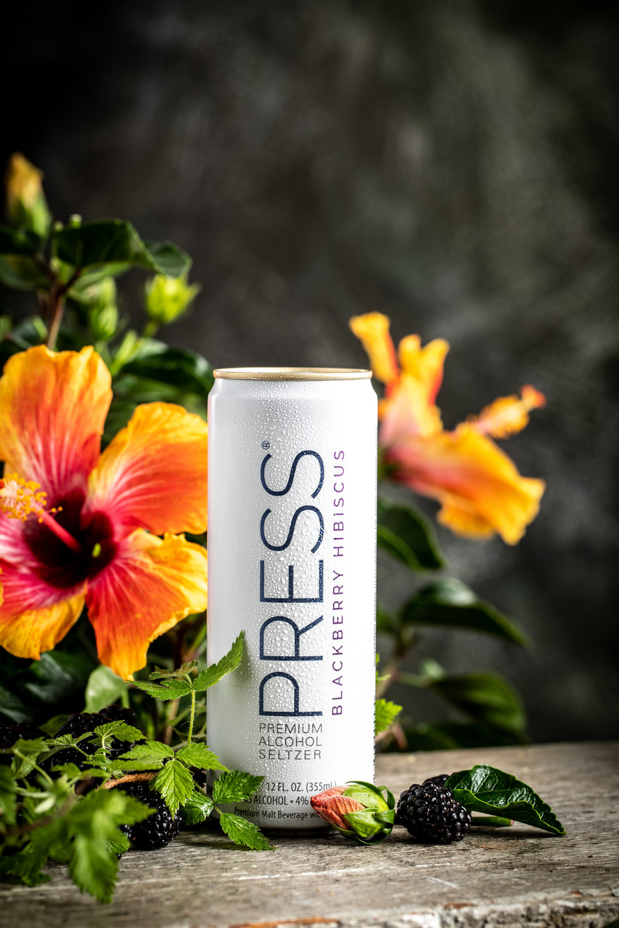Can of press seltzer taken by drink photographer with pink and orange hibiscus flowers behind. 