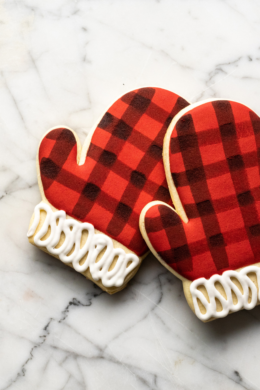 Detail of baking photography that shows the painted buffalo plaid pattern on the iced mitten-shaped cookies