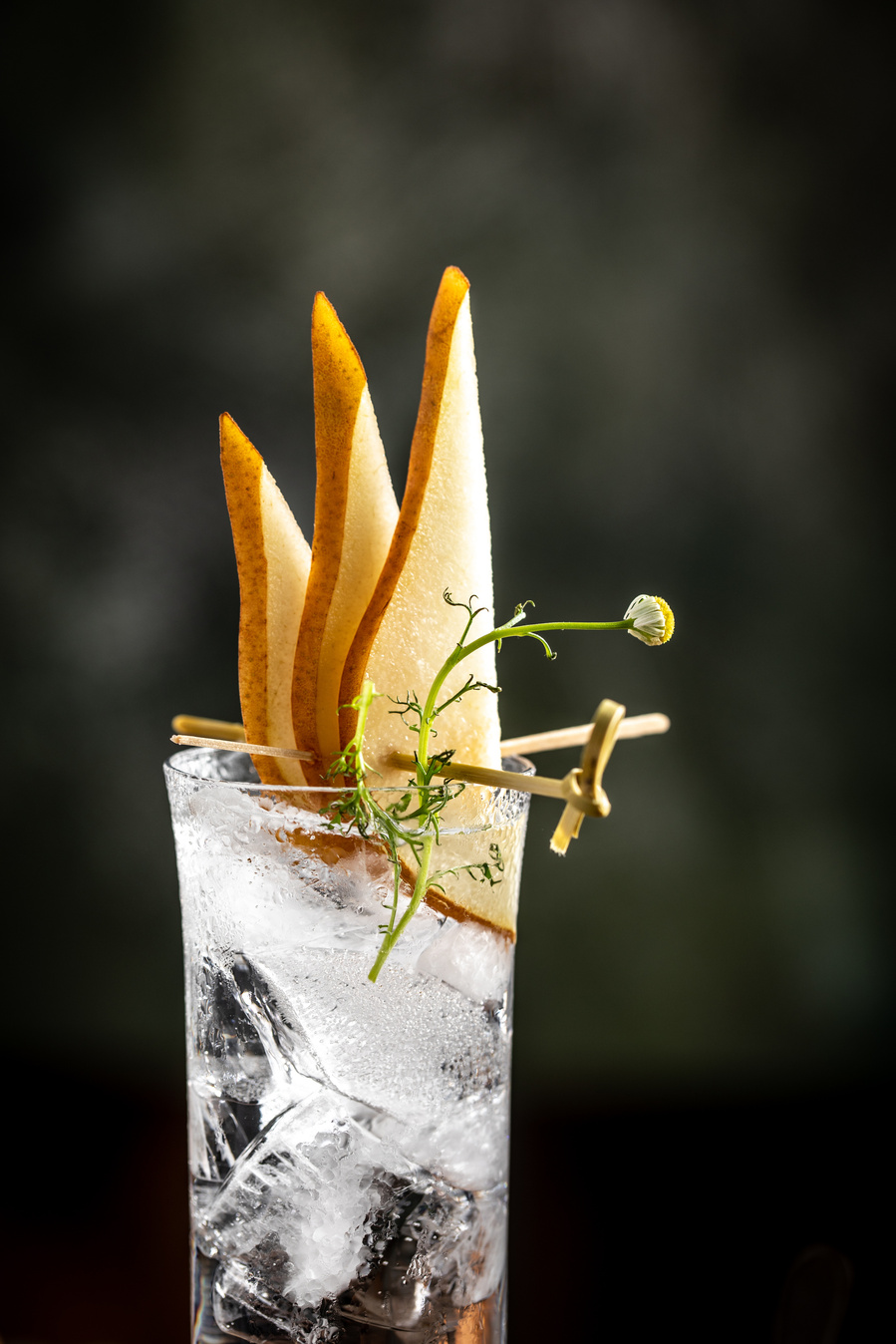 Glass with large shards of ice filled with Press Seltzer with a garnish of three pear slices and a cardamom bud. Drink photography with beautiful light