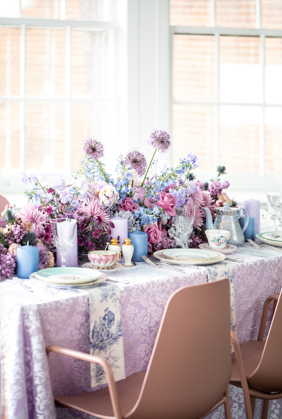An editorial photography image capturing the whimsy and charm of a Bridgeton style tea party. A table-long floral centerpiece with fine china teacups and saucers, a teapot, and small plates for the desserts.
