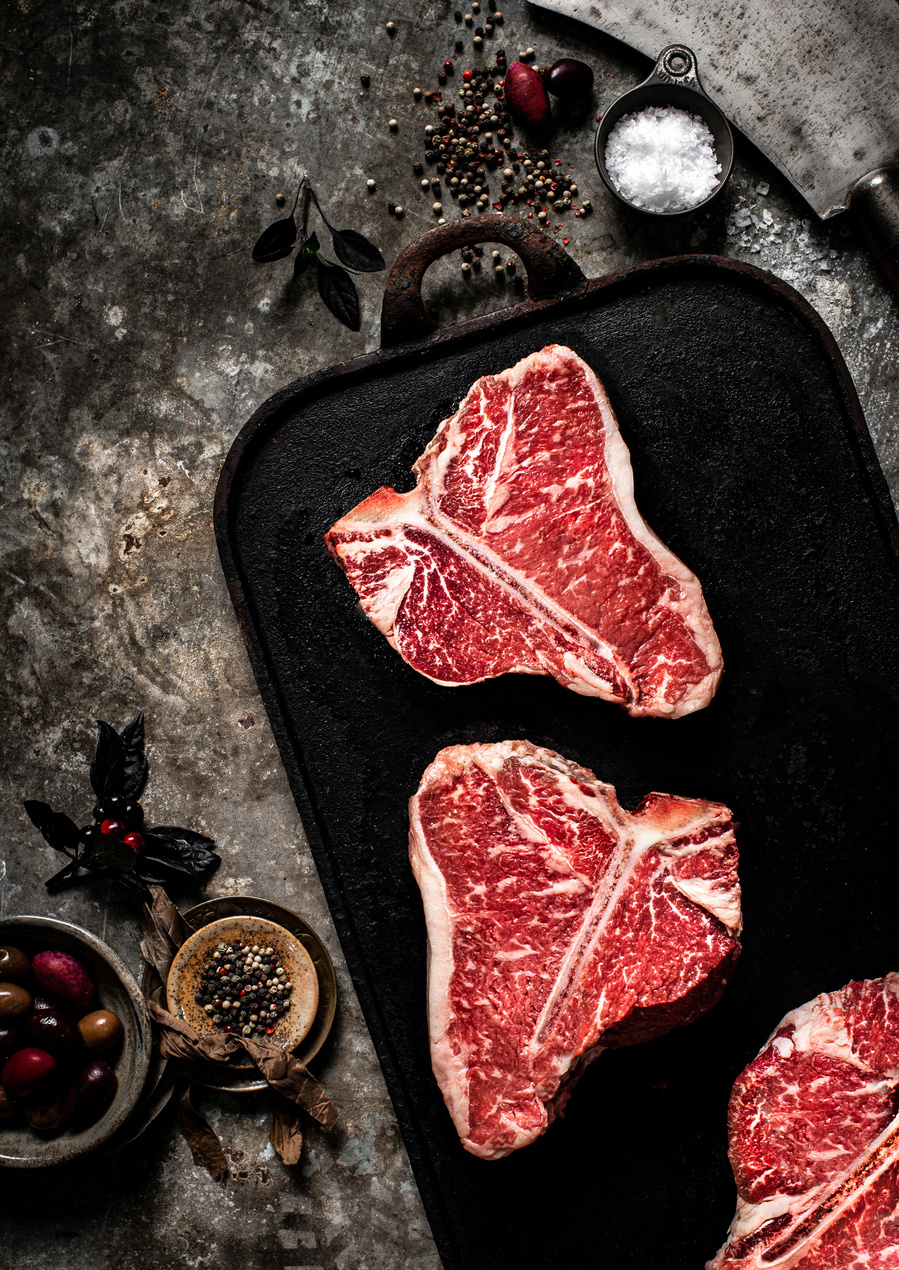 Overhead meat photography of red raw steaks on a cast iron tray with minimal props. 