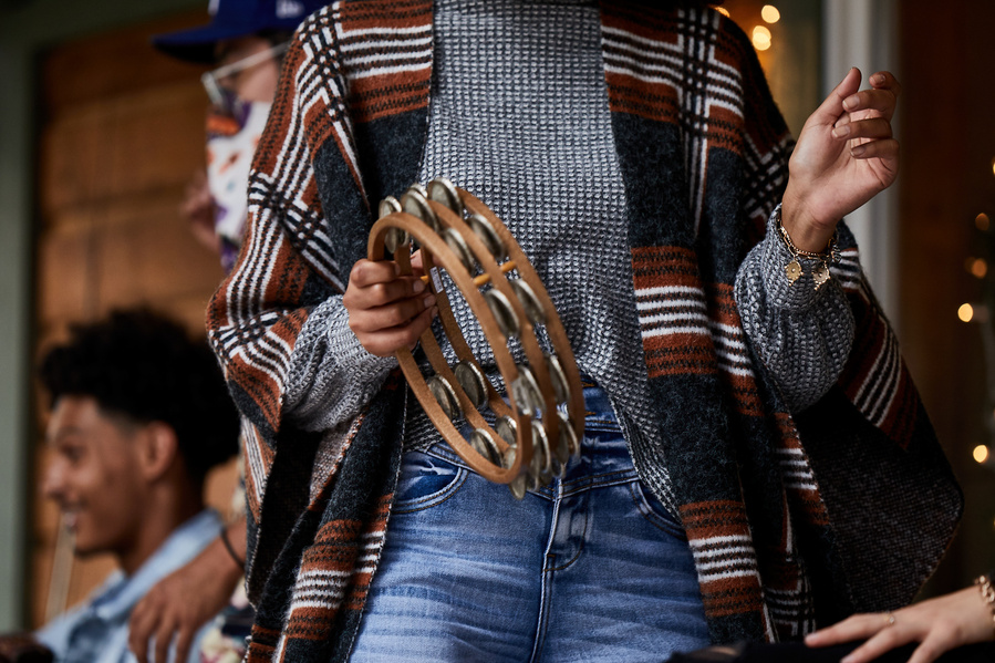 Woman in jeans and a striped flowy shrug plays tambourine on the porch with friends for lifestyle fashion photography for The Buckle 