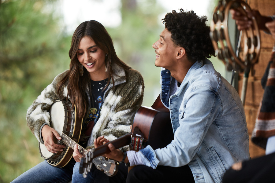 Two fashion models playing instruments on an outdoor porch in rustic fall clothing. Denim fashion photography for The Buckle
