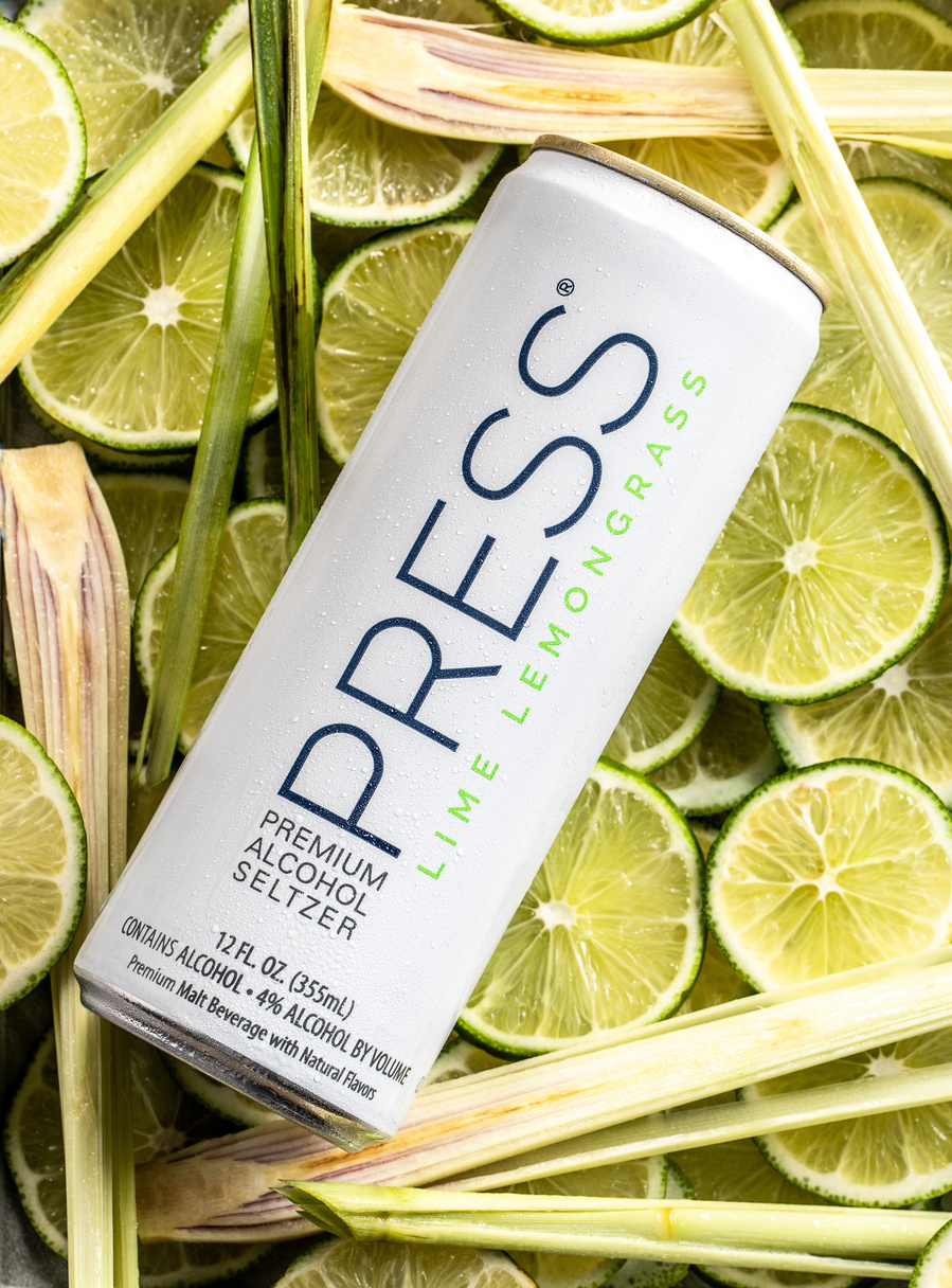 Overhead can of lime lemongrass Press seltzer laying on bed of sliced limes and lemongrass stalks. Creative drink photography 