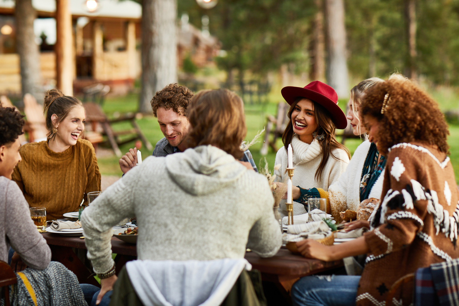 The photography of food features a group of friends gathered around a wooden table set with candles and white dinnerware. The friends are laughing and enjoying each other's company while enjoying a delicious spread of food for lifestyle food photography