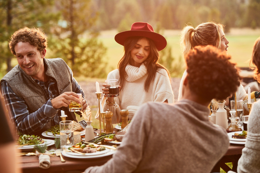 Lifestyle food photography of group of friends at an outdoor dinner party at rustic table with white a gold dinnerware. Golden hour sheds beautiful light for photography of food. 