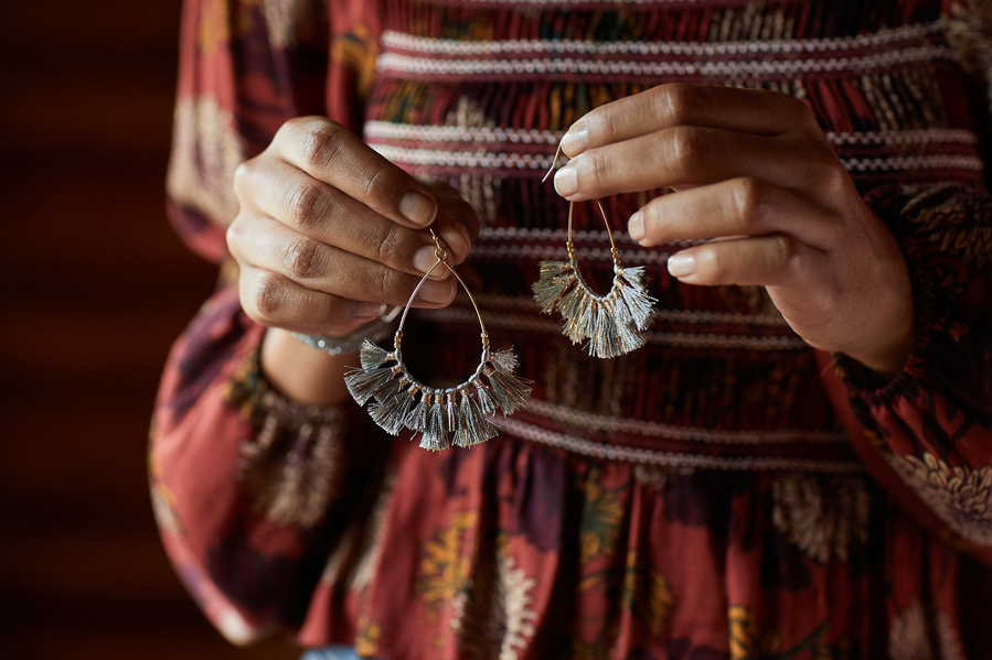 Woman holding teardrop tassel earrings in front of herself wearing red peasant blouse. Fashion lifestyle photography for The Buckle