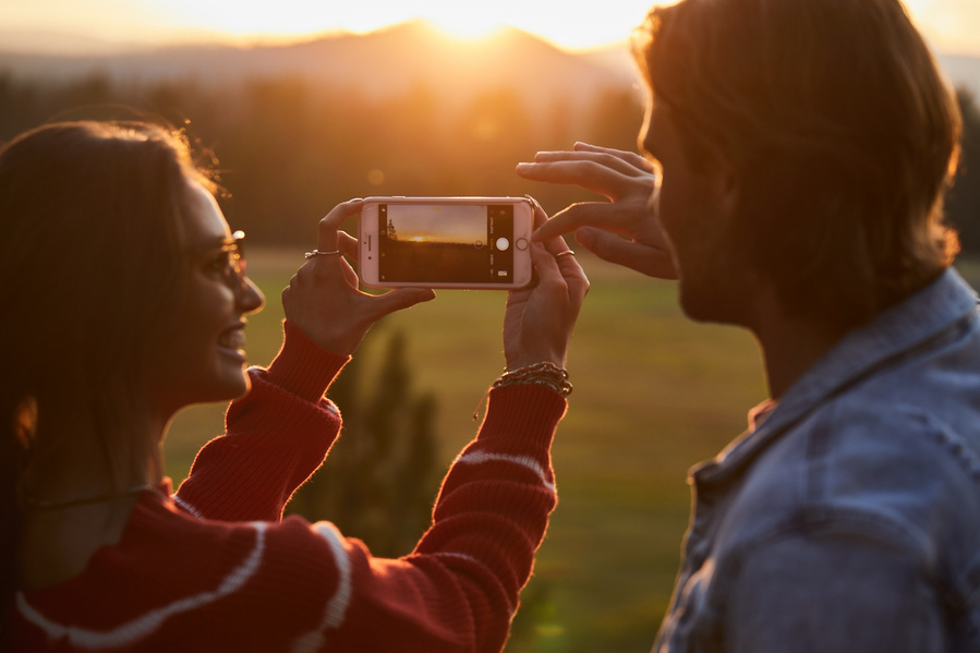 Two models in casual fall clothing take a picture of the sunset with their phone. Woman is holding the phone and looking at the man in the glow of sunset. Lifestyle Fashion Photography for The Buckle