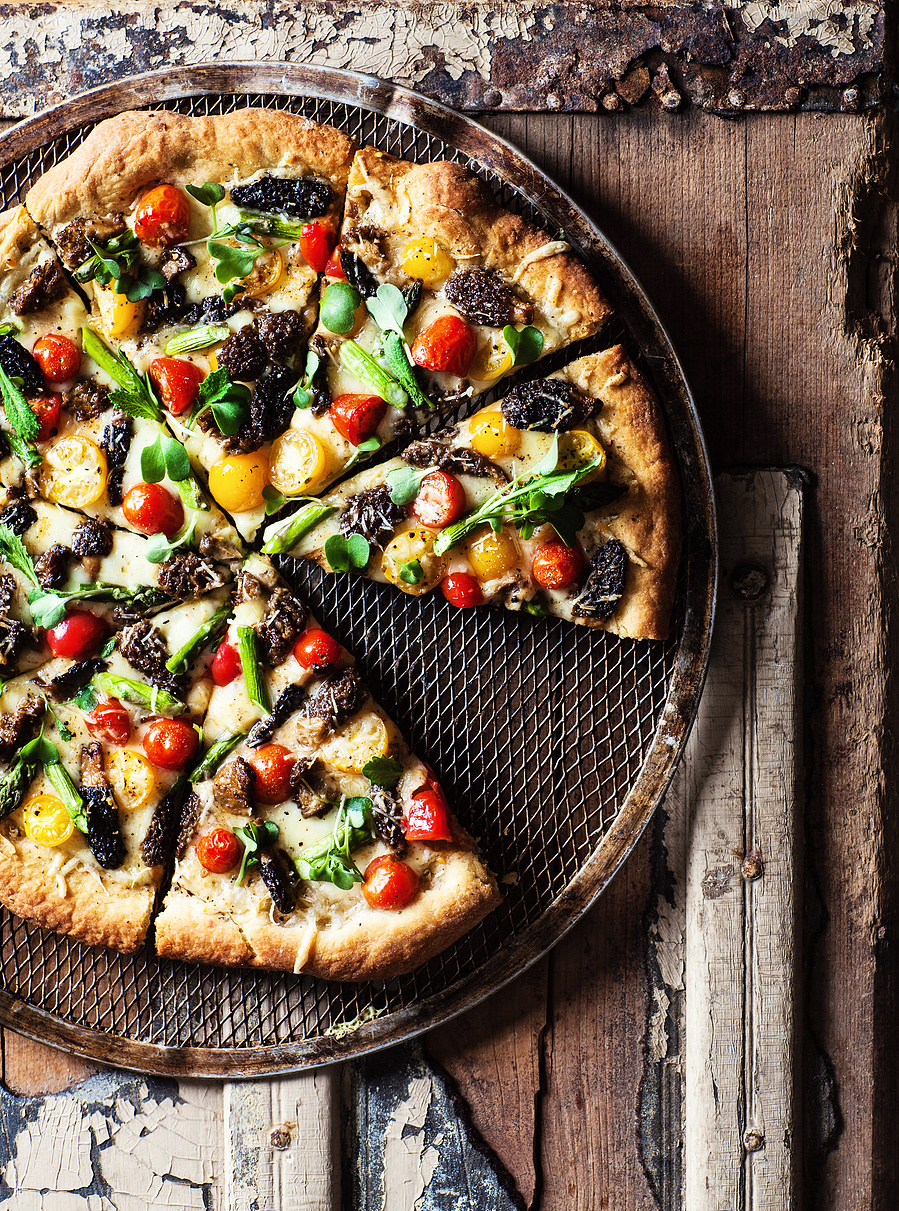 Overhead pizza photography on a rustic wooden surface. Pizza covered in bright veggies and greens. 