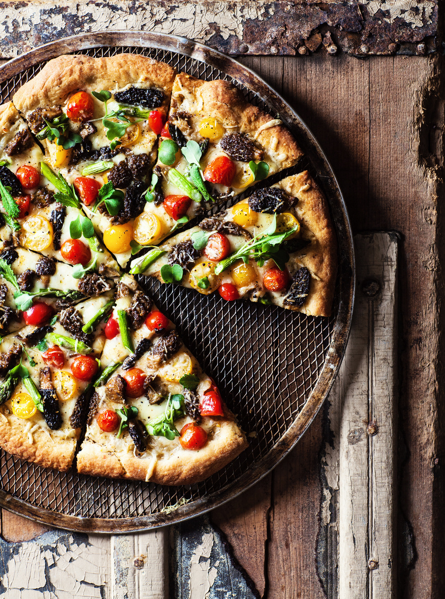 Overhead pizza photography on a rustic wooden surface. Pizza covered in bright veggies and greens. 