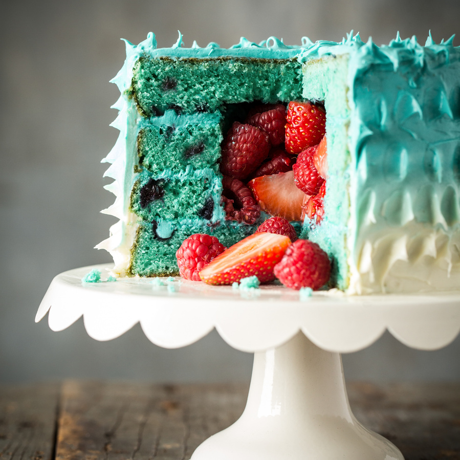 A blue and white ombre cake with strawberries pouring out of the center on a white cake plate. Cake photography for circus themed birthday party