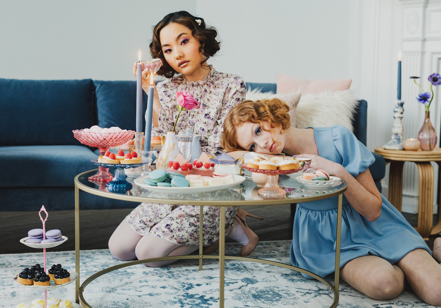 Two feminine models with cropped curls sitting at a low table with cute desserts and tea set. Editorial photography with lifestyle dessert food photography.   