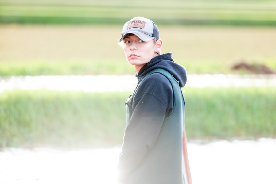 Young farmer in hat and sweatshirt standing in a flooded cranberry bog with more fields behind him. He is looking over his shoulder at the growing cranberries. Agriculture photography. 