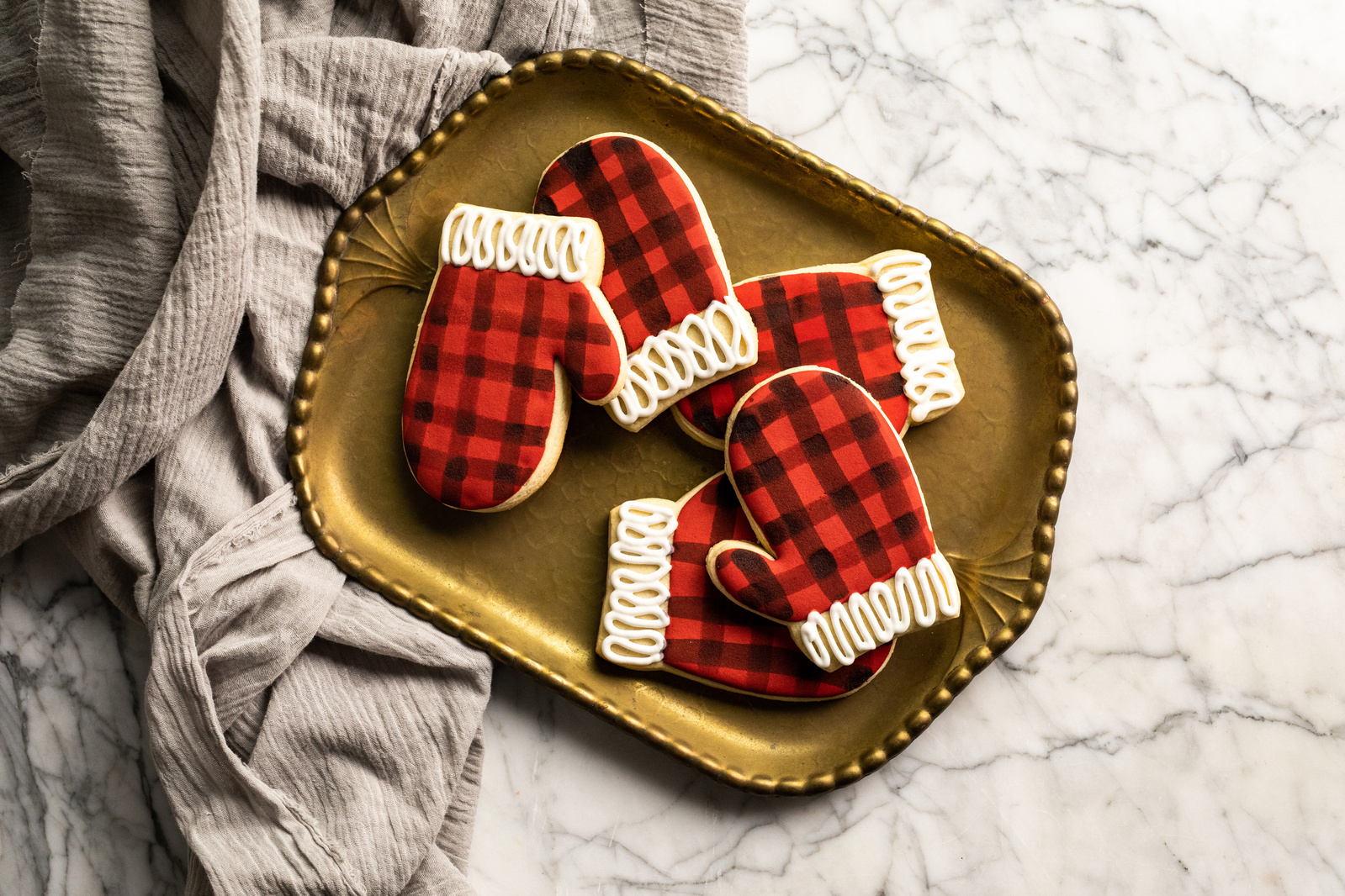 A bronze tray on marble shot as overhead baking photography with 5 buffalo check mitten cookies as part of brand photography for Maurices