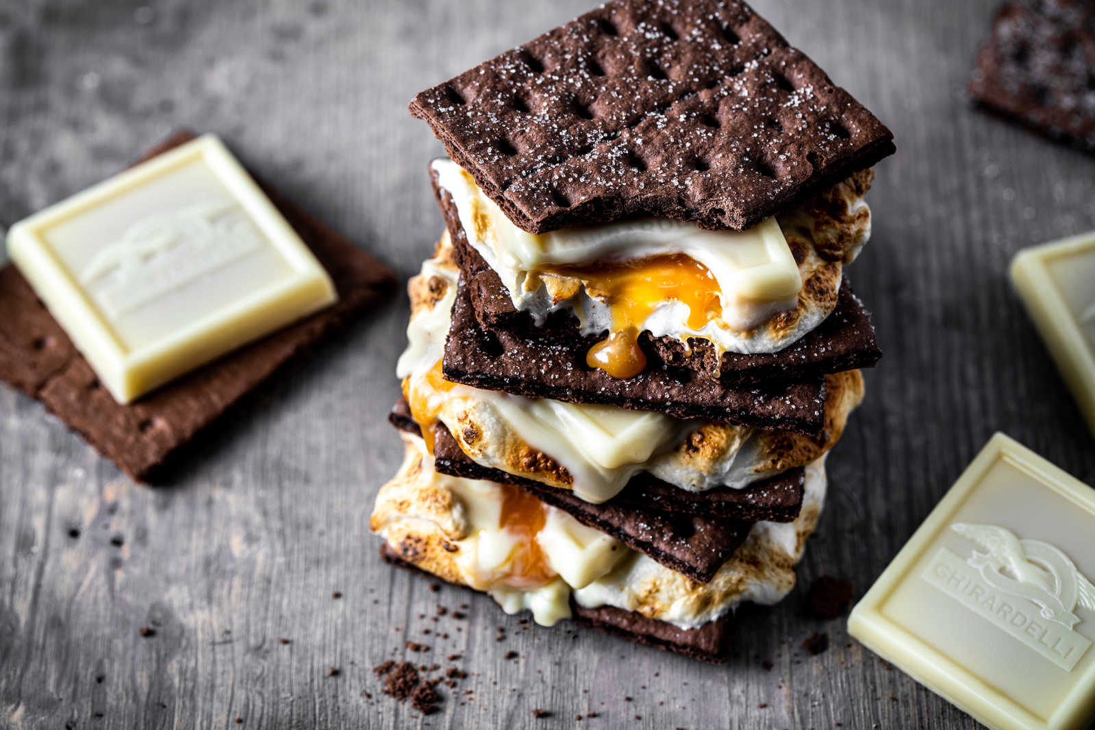 A melty drippy three-layer s'more with chocolate graham crackers and Ghirardelli white chocolate caramel squares. Moody food photography. 
