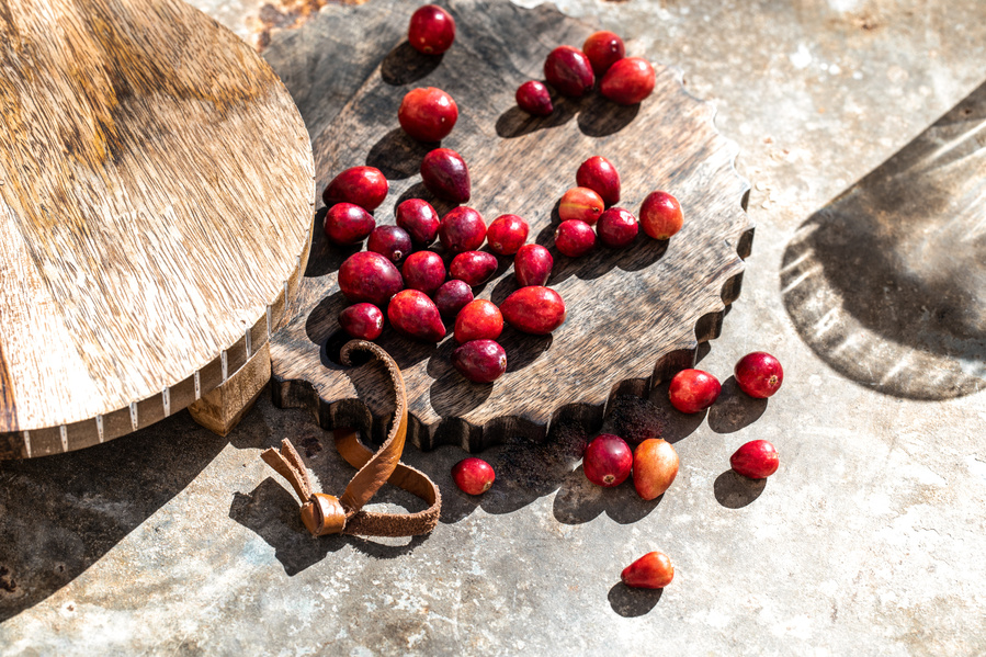 Loose cranberries on a rusted surface with two wooden pedestals and shadow of sun through a water glass creative food photography