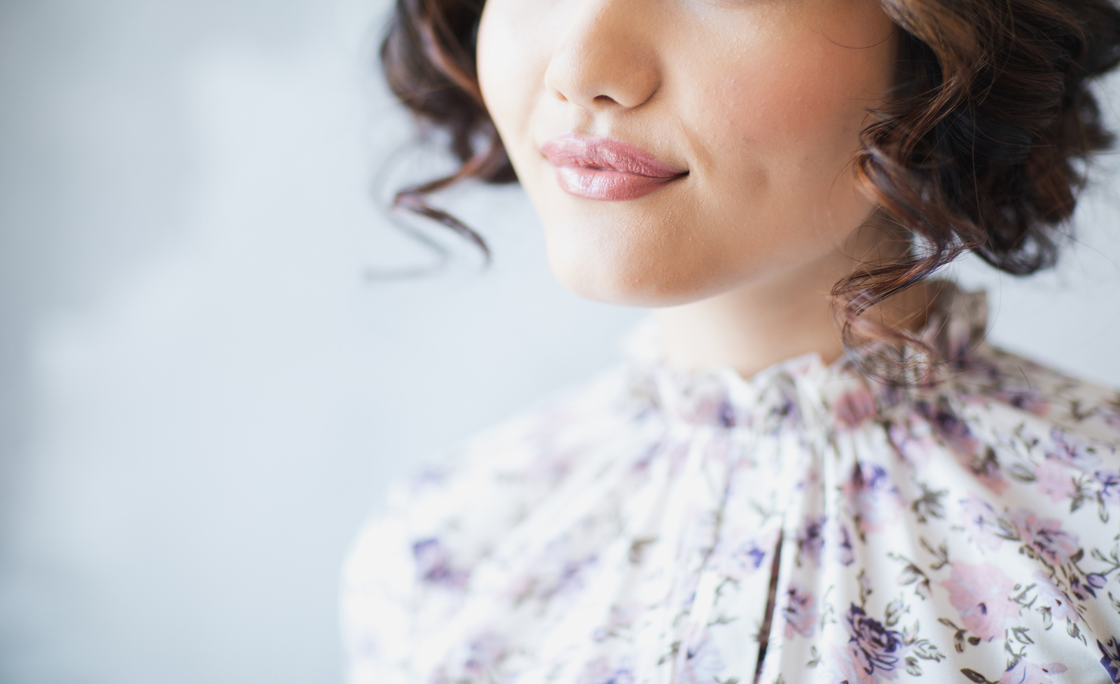 Cropped closeup of model in floral high-neck top with pink lips and brown bobbed curly hair. An editorial photography image with a model from a Bridgeton style tea party.