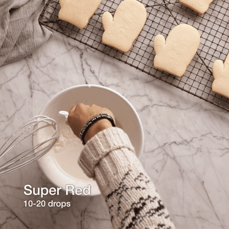 Baking photography progress video gif of dying white icing in a white bowl red, then piping an icing outline around the edge of the mitten-shaped cookie. 