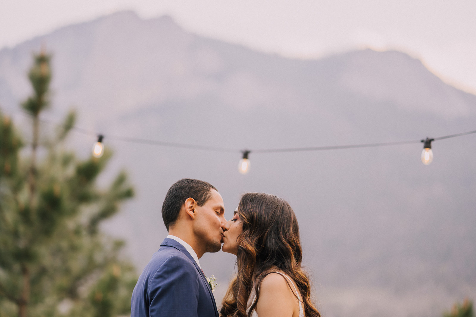 Bride and groom kissing in front of mountains, Della Terra Mountain Chateau.