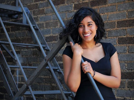 Indian American young woman in black sweetheart neckline dress smiling and holding onto stair rail