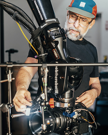 Director and photographer Timothy Hogan calibrating a motion control camera rig using a cinema robot for high-speed tabletop cinematography. Featuring gear like the Camerabotics arm, with a cinema lens setup,