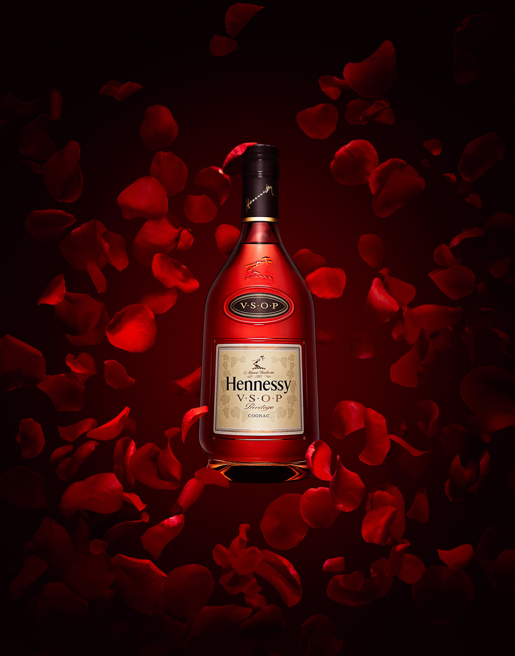 Bottle of Hennessy VSOP Cognac on deep red background with floating rose petals photographed by Timothy Hogan. 
