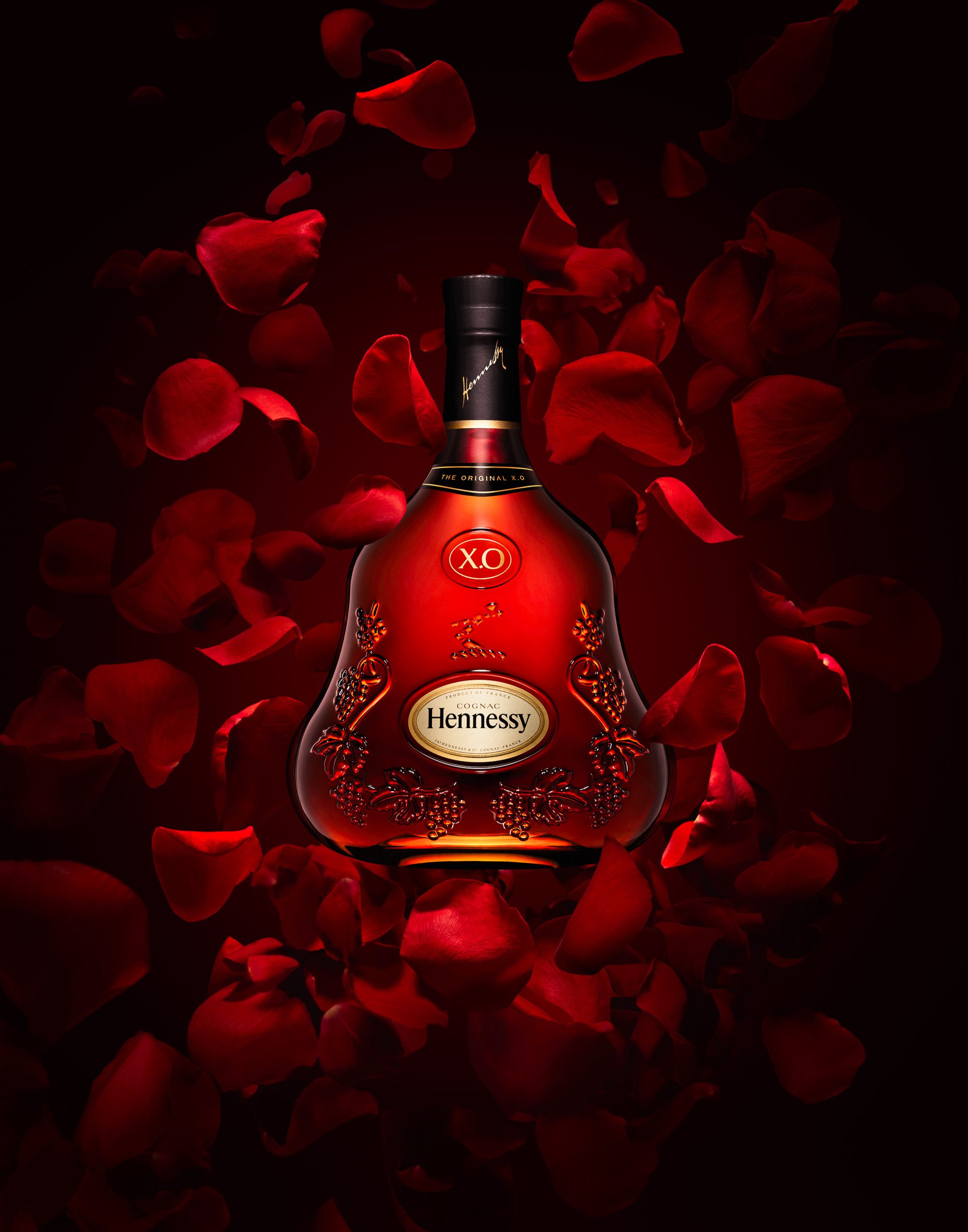 Bottle of Hennessy XO Cognac on deep red background with floating rose petals photographed by Timothy Hogan. 