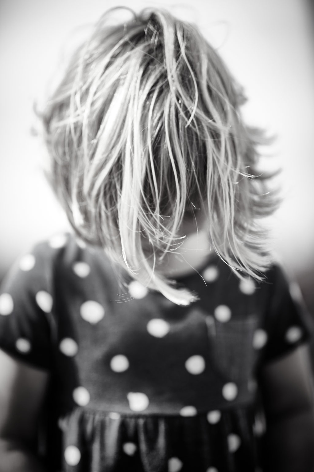 Black and white portrait of a child looking down with her hair over her face. She is wearing a polka-dot dress. Shot by Norwich commercial, freelance portrait photographer Matt Keal.