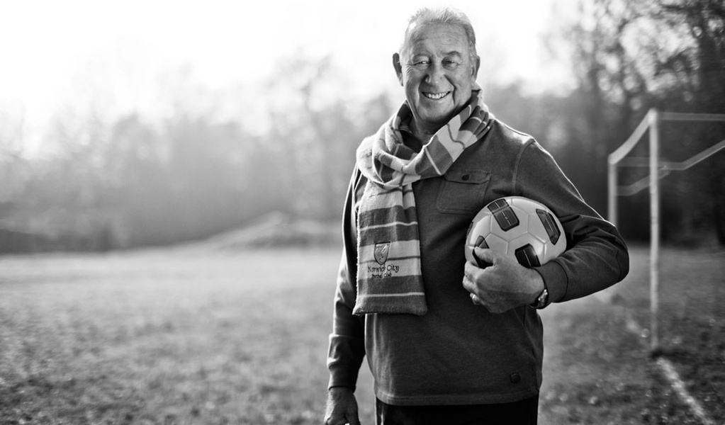 Black & white portrait of a football club manager standing outside holding a football and wearing a Norwich City Football Club scarf. Shot by Norfolk commercial, freelance portrait photographer Matt Keal.