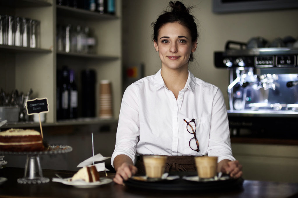 Meet the team photo of a coffee shop employee wearing a white shirt and carrying drinks and cake. Shot by Norwich commercial, freelance portrait photographer Matt Keal.