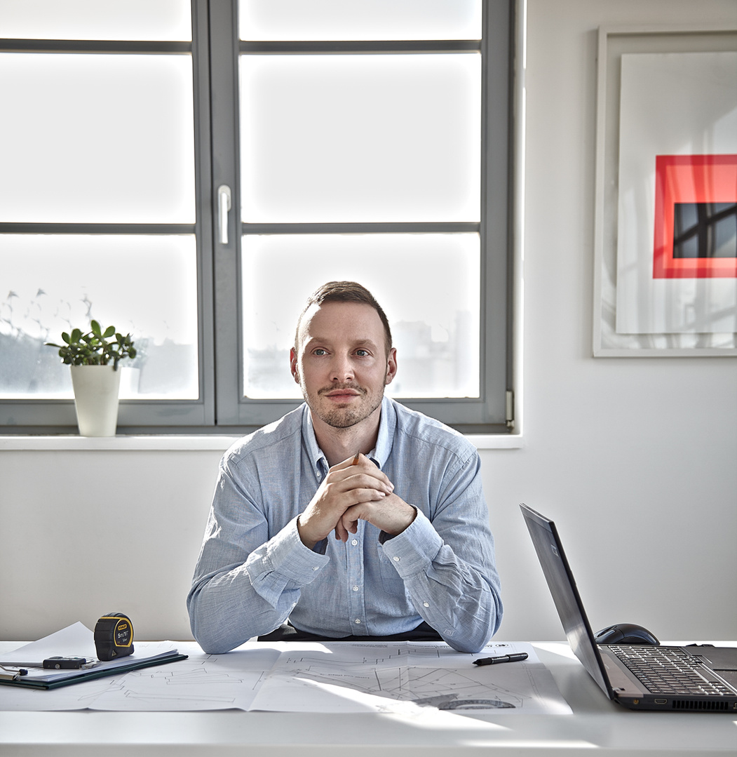 Portrait of an architect sitting at a desk in an office with a window behind. Shot by Norwich commercial, freelance portrait photographer Matt Keal.